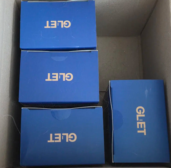 푸른색 패키지 박스에 담긴 지엘어트 유산균 제품. 박스 디자인에 GLET 로고가 인쇄되어 있으며, 택배 상자 안에 정리된 모습.